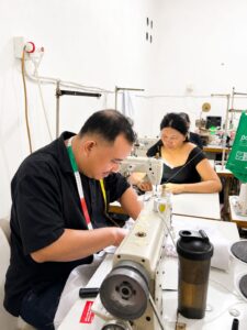 Professional male tailor focused on sewing fabric using an industrial sewing machine at MARI Garment factory in Bali.