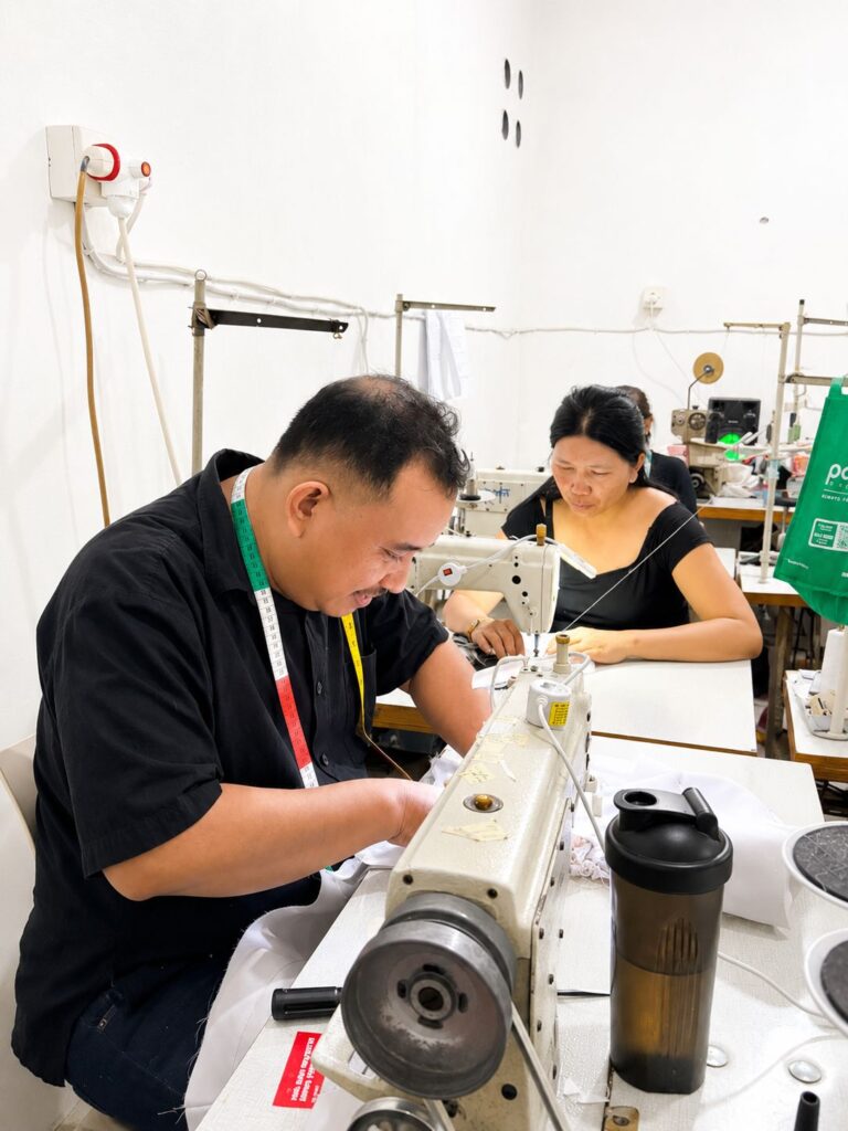 Professional male tailor focused on sewing fabric using an industrial sewing machine at MARI Garment factory in Bali.