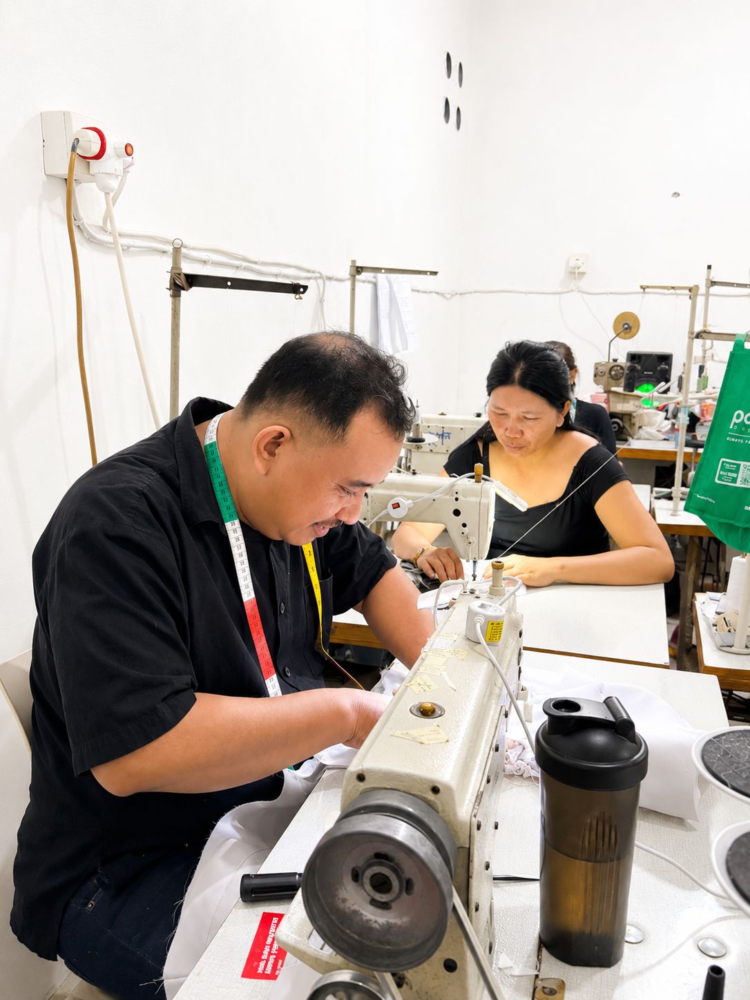 Professional male tailor focused on sewing fabric using an industrial sewing machine at MARI Garment factory in Bali.
