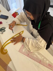 Skilled pattern maker using a French curve ruler to draft precise clothing patterns at MARI Stitch manufacturer workshop in Bali.