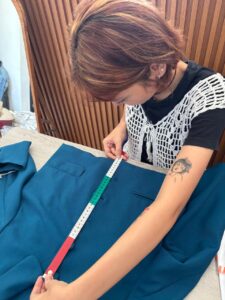 Creative team member precisely measuring a teal blazer with a tape measure, ensuring high-quality clothing production at MARI Garment Bali.