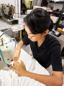 Experienced seamstress carefully sewing intricate white pleated fabric on a sewing machine for premium garment production in Bali.