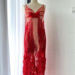 Elegant sheer red dress with intricate floral appliques on a mannequin, custom produced by MARI Garment manufacturer in Bali.