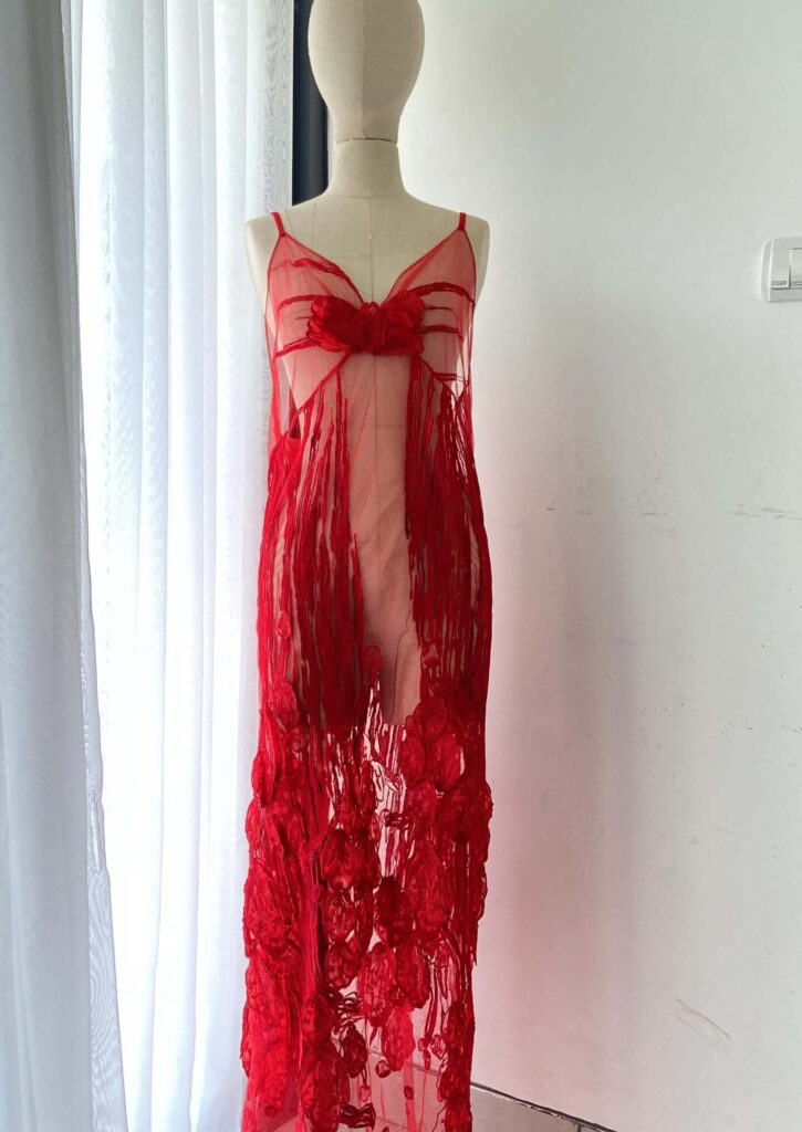 Elegant sheer red dress with intricate floral appliques on a mannequin, custom produced by MARI Garment manufacturer in Bali.