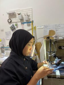 Dedicated tailor operating a sewing machine to stitch a blue striped garment at MARI Garment manufacturing studio in Bali.